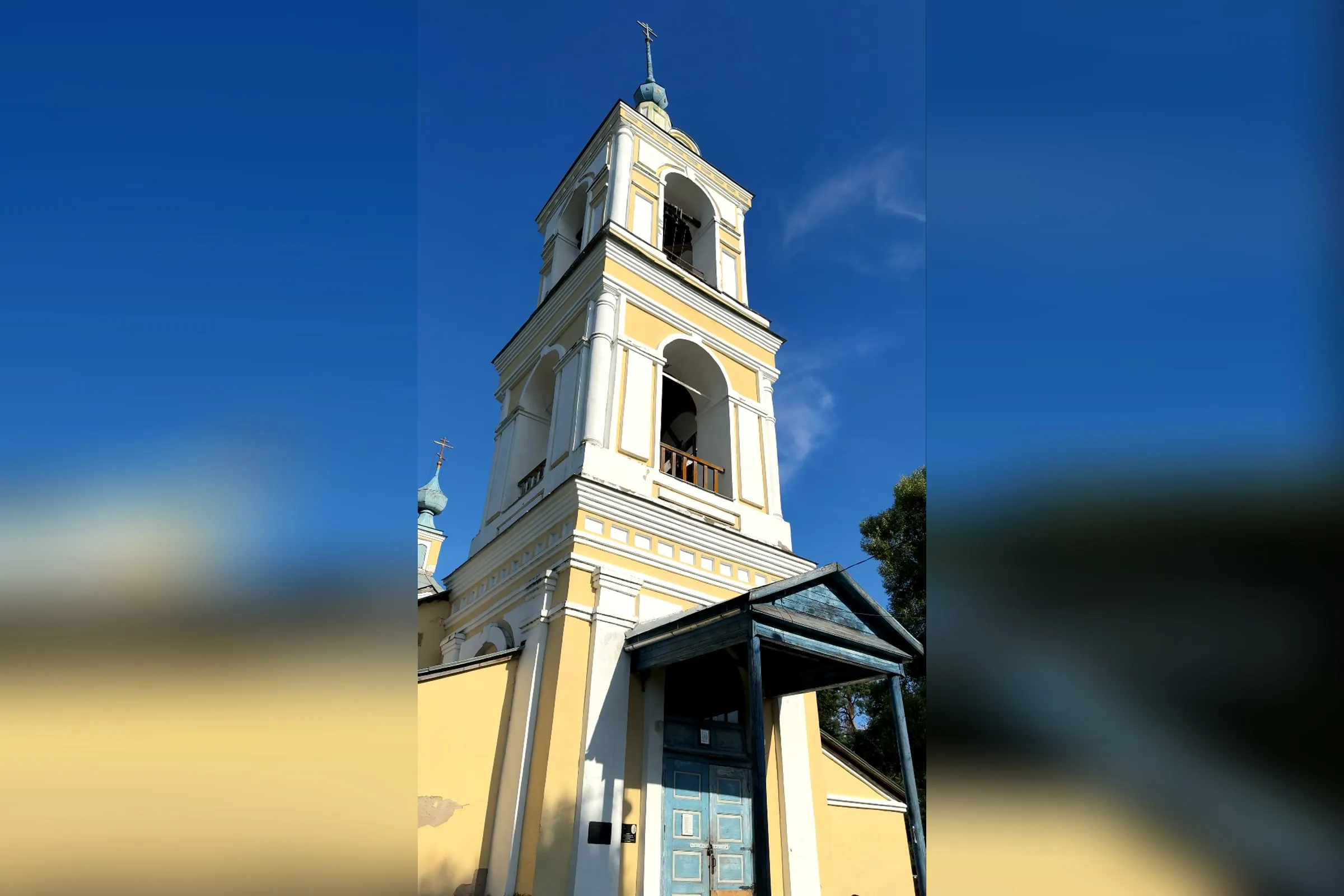 Жёлто-белая колокольня Троицкой церкви в селе Троицкое на Устье, внизу синее деревянное крыльцо