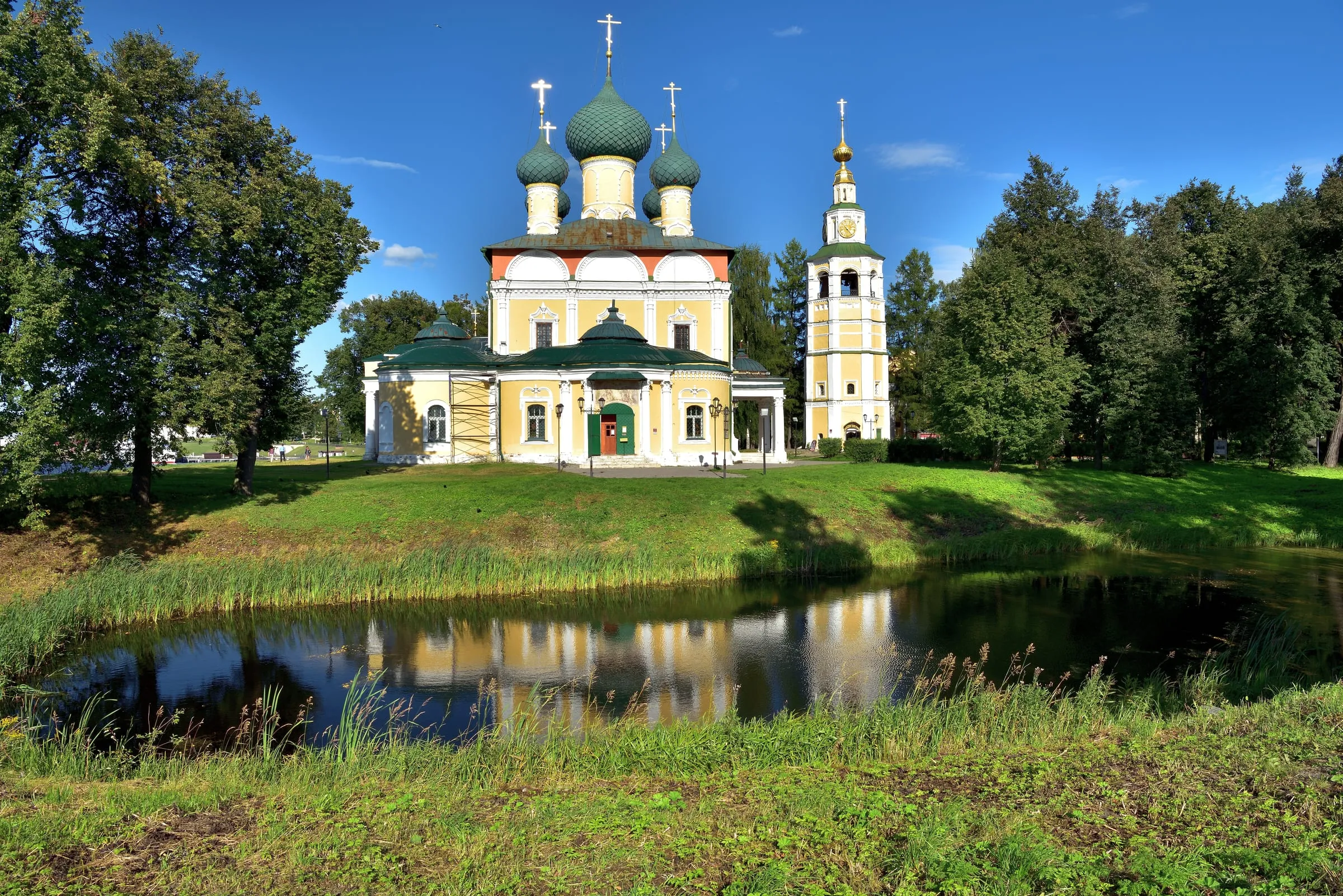 Die Verklärungskathedrale im Kreml von Uglitsch mit grünen Kuppeln und gelbem Glockenturm, davor spiegelt ein Teich das Ensemble