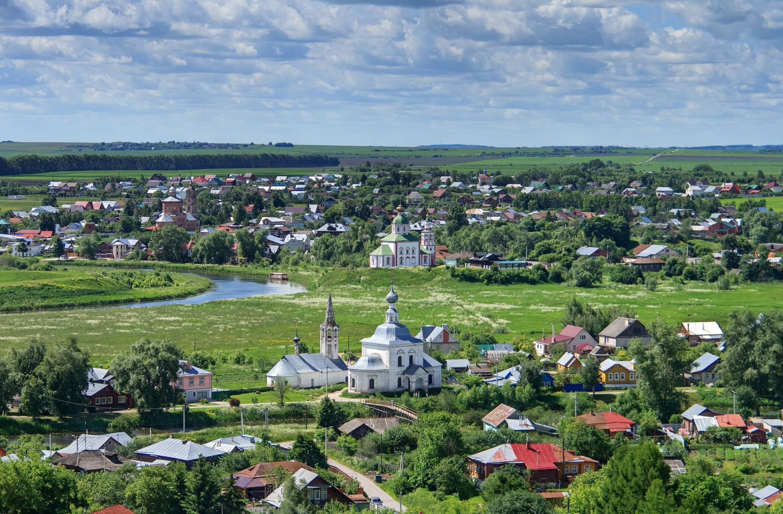 Panorama von Susdal mit weißen Kirchen, Holzhäusern und grünen Wiesen unter weitem Wolkenhimmel